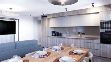 A modern kitchen with built-in appliances, a dining area with a wooden table set for six, and a grey sofa in the living area.