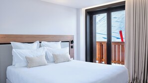 Une chambre d’hôtel avec un grand lit, une tête de lit en bois et une vue sur un balcon où se trouve une chaise rouge.
