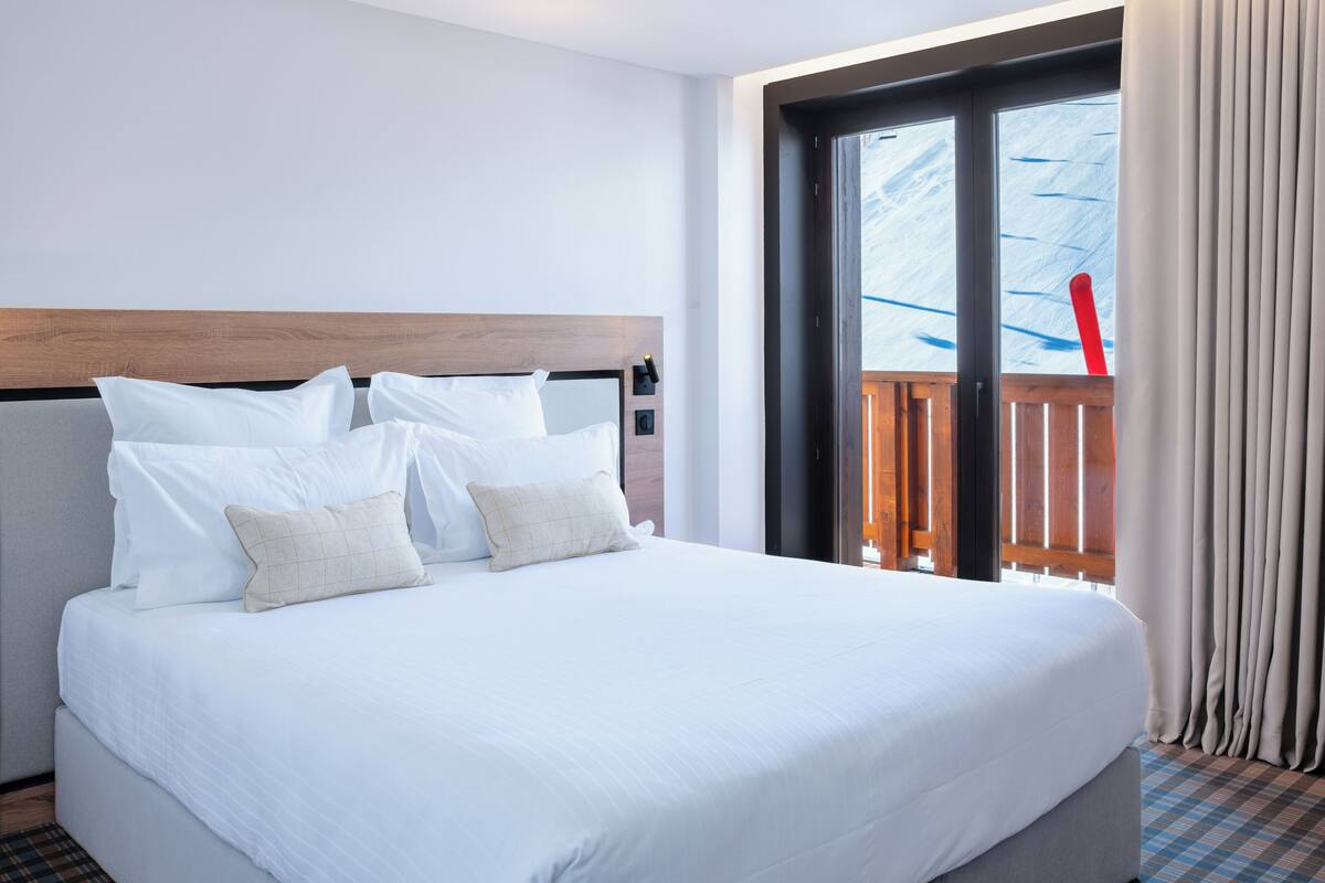 Een hotelkamer met een groot bed, een houten hoofdbord en uitzicht op een balkon met een rode stoel.