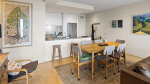 A modern kitchen with white cabinets, a stainless steel refrigerator, and a dining area with a wooden table and chairs. - Ocean Views, 2 Bedroom Apartment (San Remo)