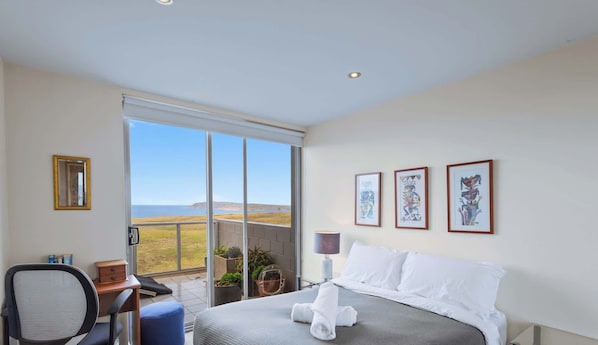 Ein Hotelzimmer mit einem Bett, einem Schreibtisch, einem Sessel, einem großen Fenster und drei gerahmten Kunstwerken an der Wand.