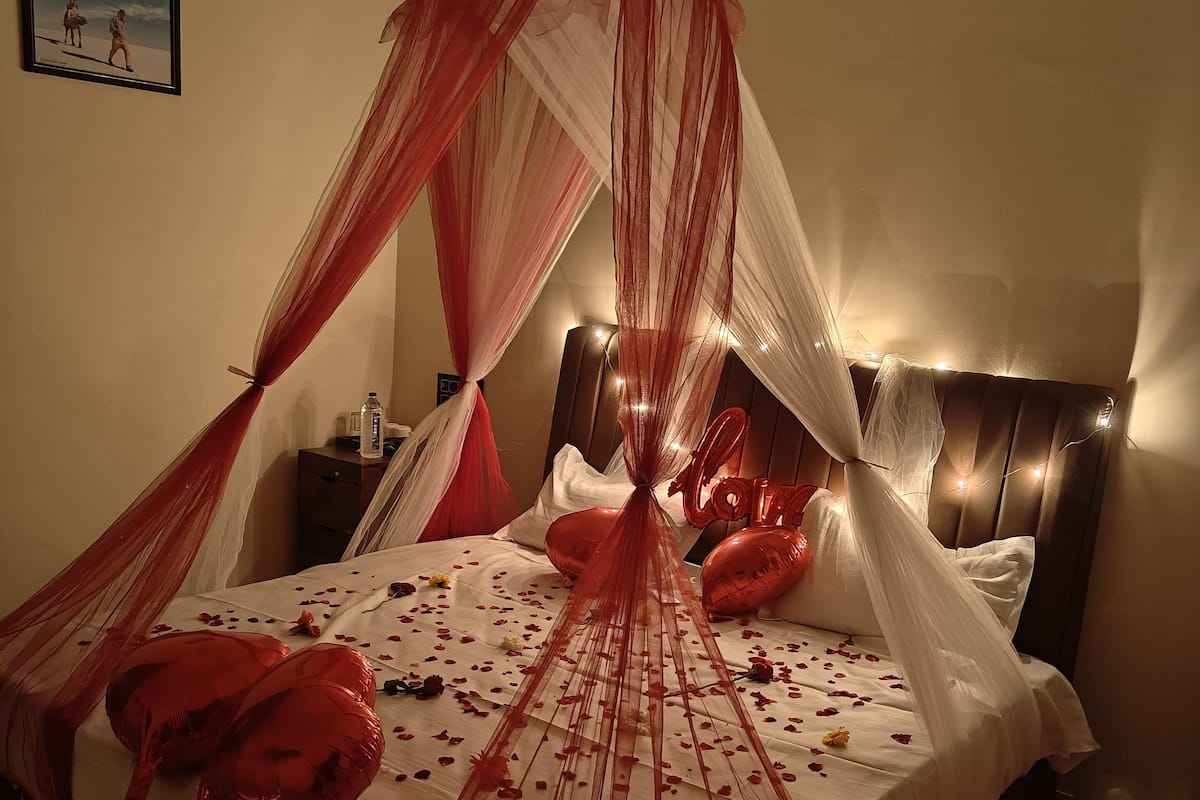 Un lit à baldaquin, des ballons et des pétales de rose.