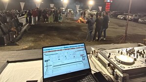 A DJ setup with a laptop and turntables, surrounded by a crowd and stage lights. - Sky View Resort (Bhuj)