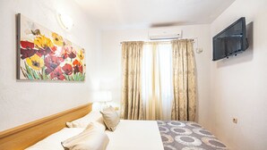 Quarto de hotel com cama, um quadro, cortinas, uma televisão e um aparelho de ar condicionado.