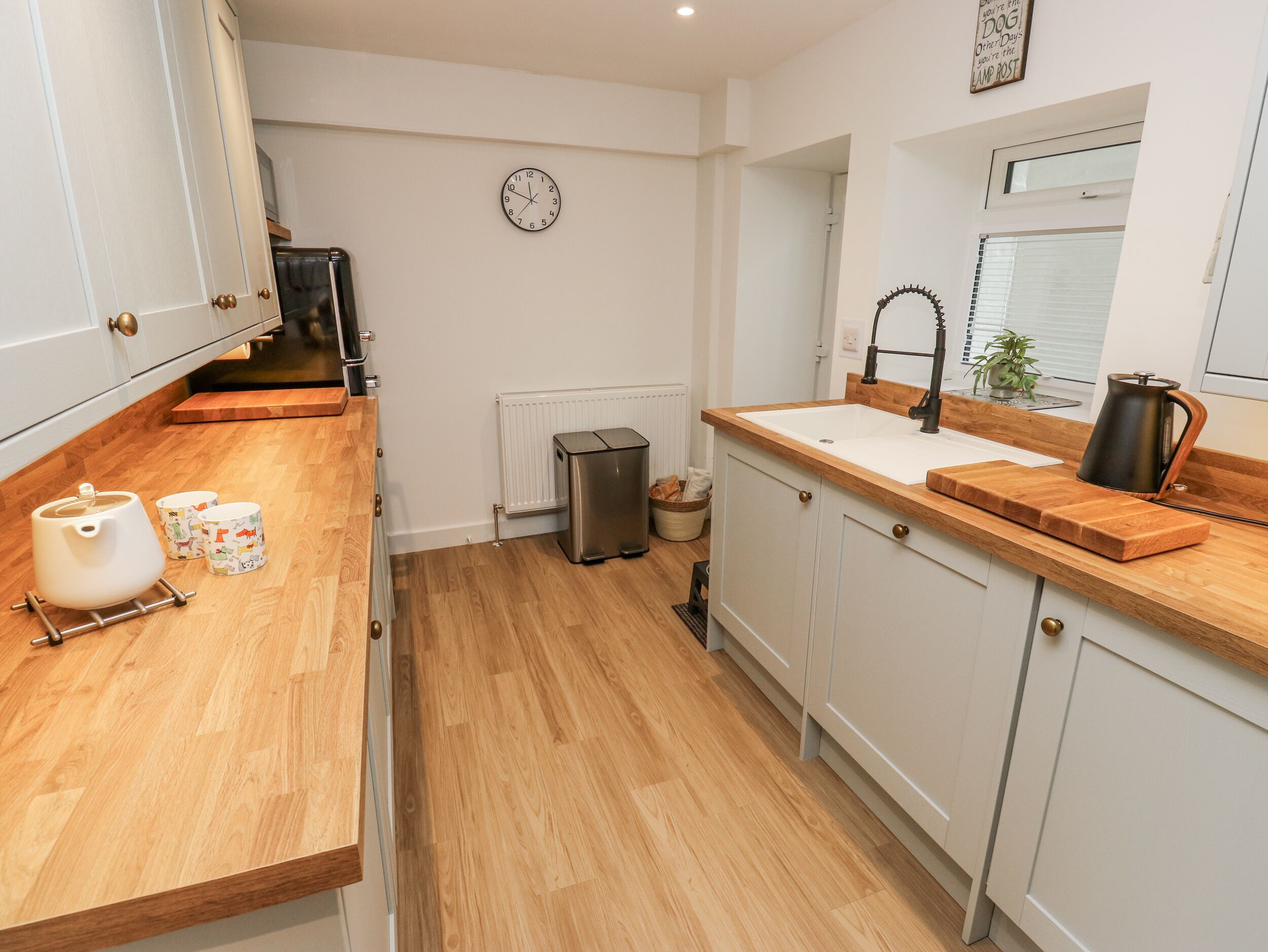 Une cuisine moderne avec des armoires blanches, un plan de travail en bois, un évier, une bouilloire et une horloge au mur.