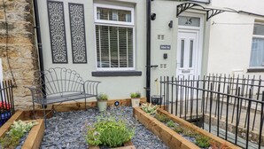 A courtyard with a wooden bench, potted plants, and a black metal fence. - Millside View (Keighley)