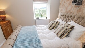 A bedroom with a bed, a bedside table, a lamp, a window, and a projector. - Millside View (Keighley)