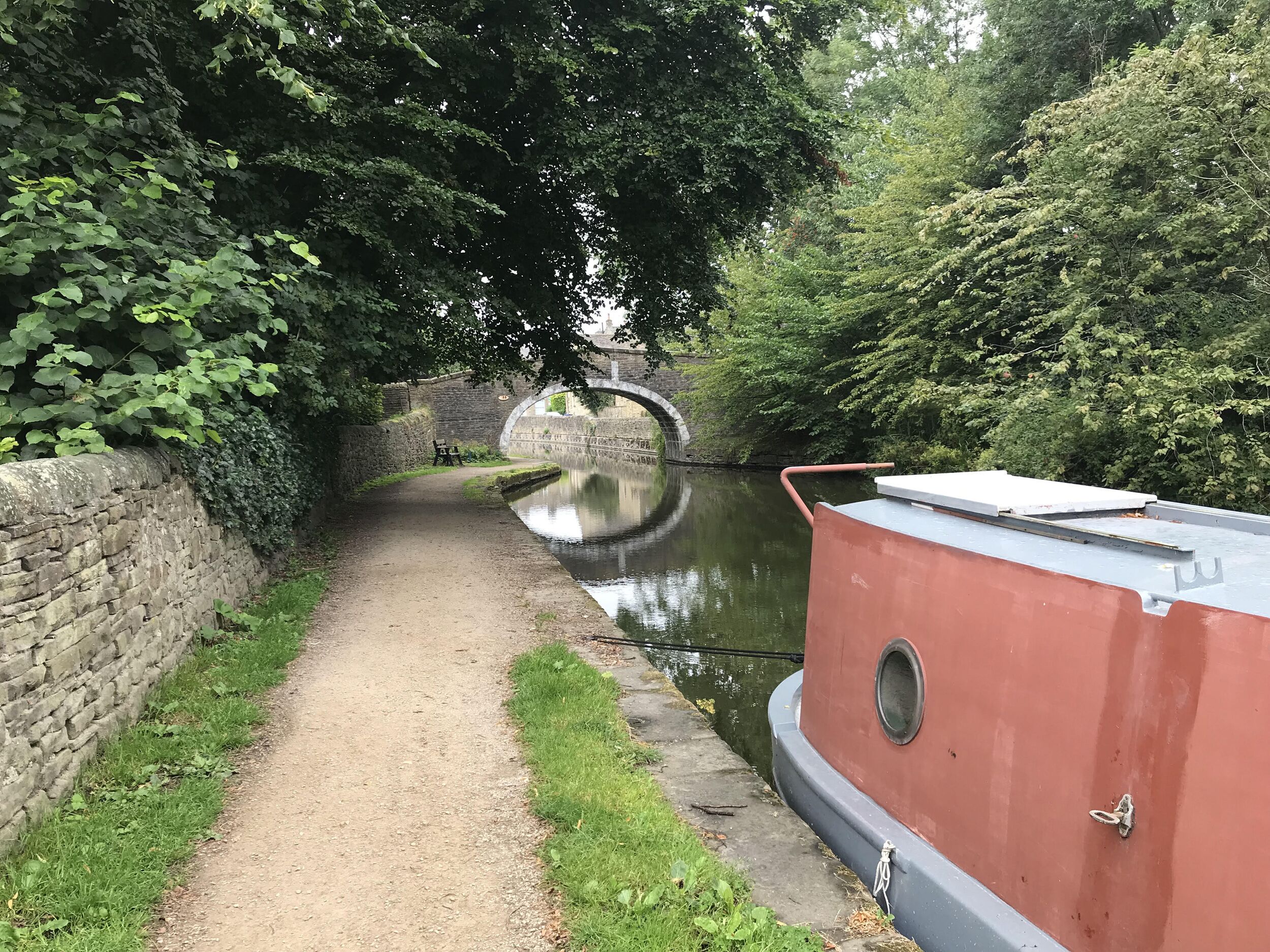A narrow canal path with a stone wall on one side and a red boat docked on the other.