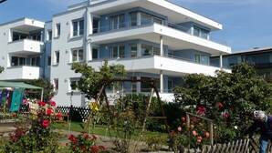 Un edificio a più piani con balconi, un giardino con rose e un'altalena.