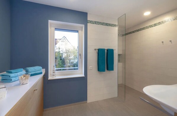 A bathroom with a bathtub, a shower area, a window with a view, and a towel rack with two towels.