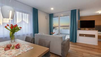 Ein modernes Wohnzimmer mit Esstisch, Sofa und einem an der Wand befestigten Fernseher.