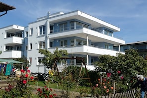 A multi-story building with balconies, a garden with roses, and a swing set.