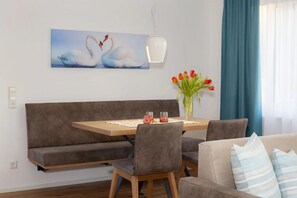 Un coin repas avec une table en bois, un canapé gris à revêtement en tissu et des chaises. Un vase avec des fleurs rouges est posé sur la table.