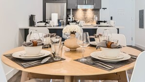 A dining area with a round table set for two, featuring white plates, clear glasses, and a vase with white flowers.