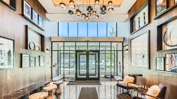A modern lobby with a glass door entrance, wooden paneling, and a chandelier.