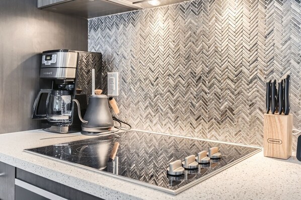 Una cocina moderna con salpicadero de diseño en espiga, estufa empotrada, cafetera y bloque para cuchillos.