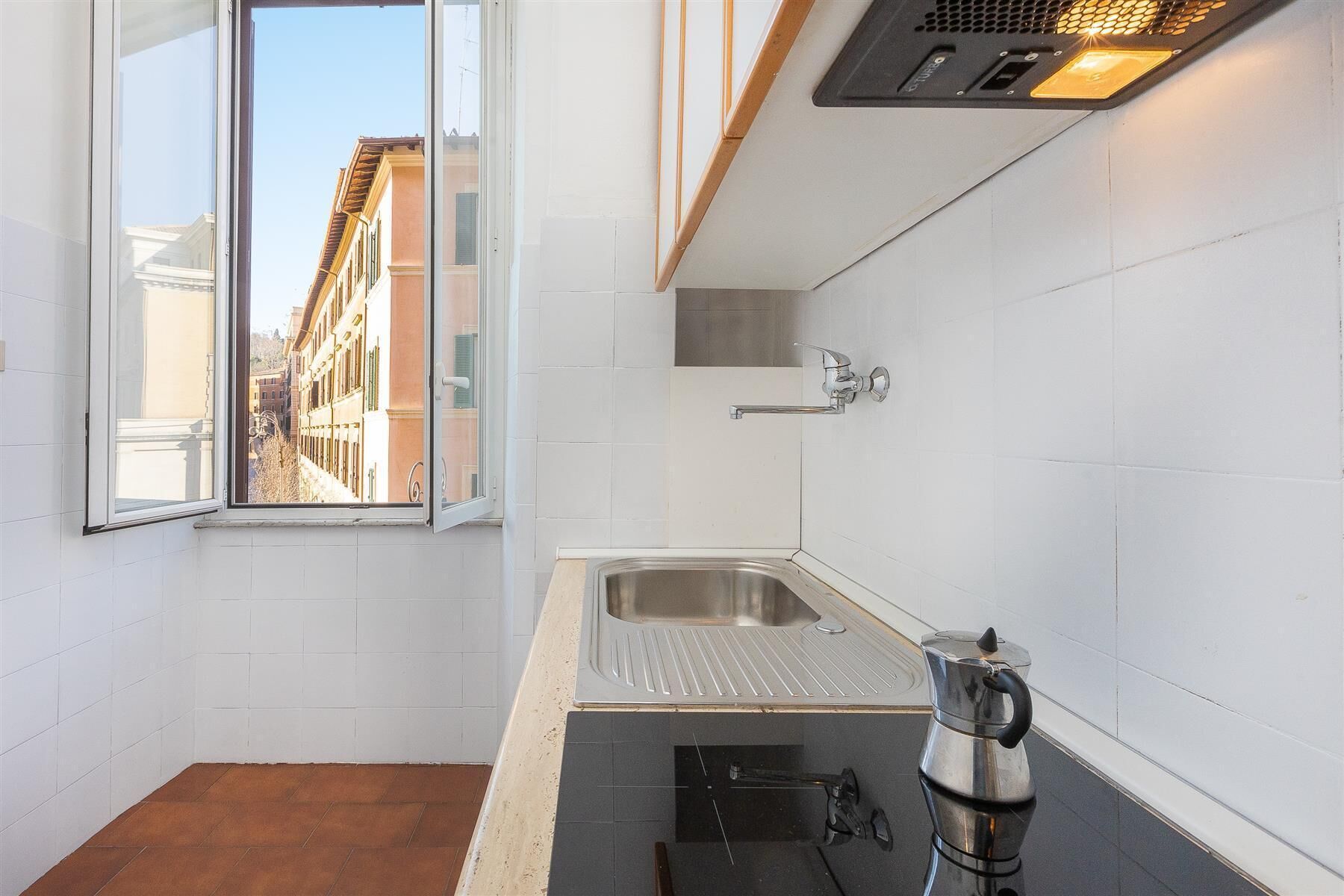 A small kitchen with a window, a sink, a kettle, and a ventilation hood.