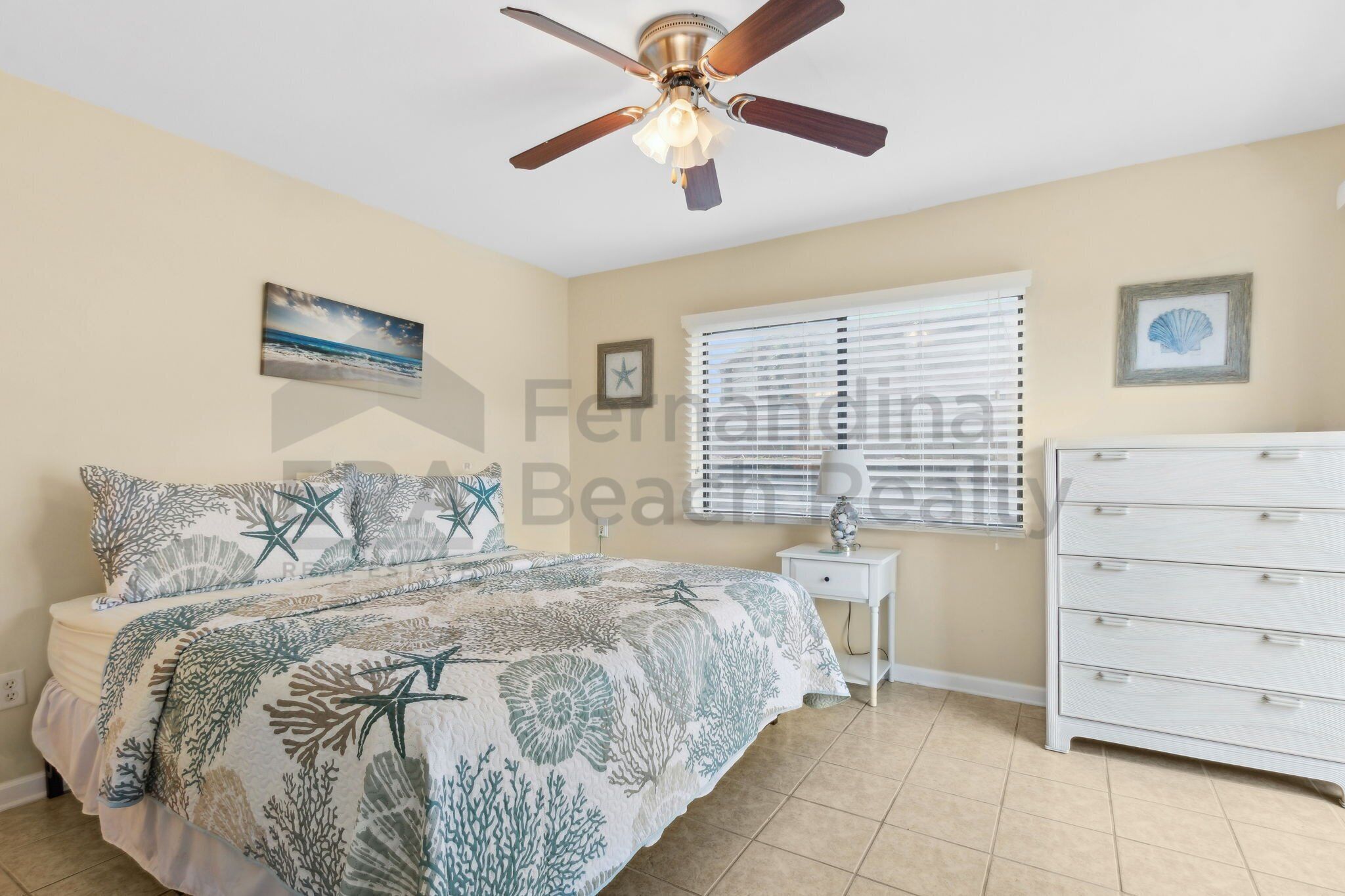 A bedroom with a bed, a ceiling fan, a nightstand, a dresser, and a window with blinds.