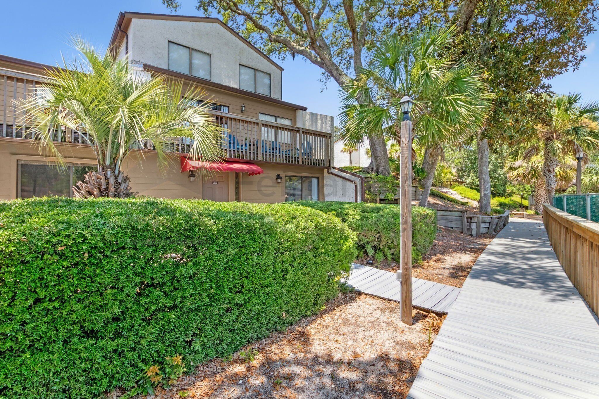 A modern building with a balcony, surrounded by well-maintained greenery and a wooden pathway.
