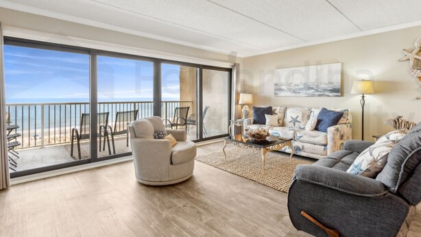 A spacious living room with a balcony overlooking the beach, furnished with a sofa, armchairs, and a coffee table. - 667 Amelia By The Sea 3 Bedroom Condo (Fernandina Beach)