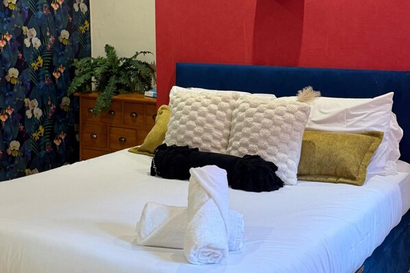 A neatly made bed with white linens, a blue headboard, and multiple pillows in various colors.