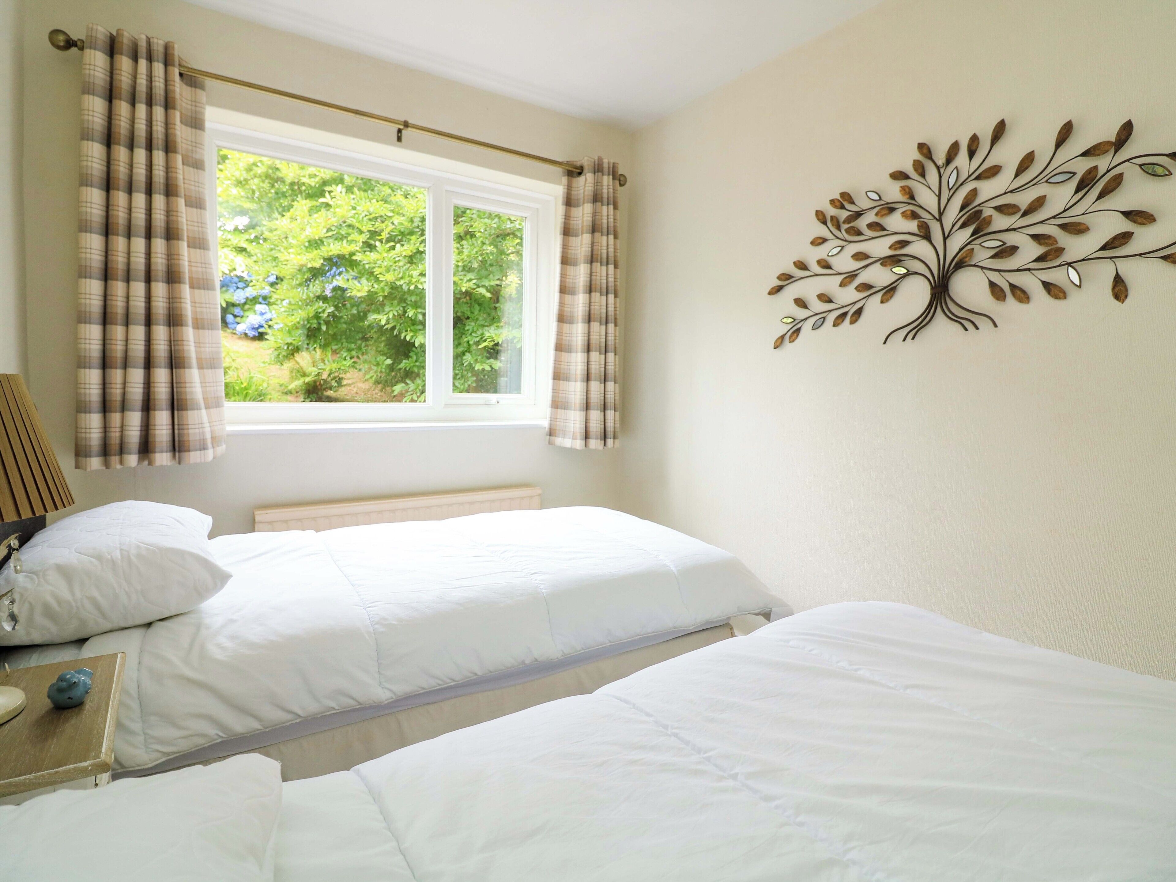 A bedroom with two beds, a window with curtains, a bedside lamp, and a wall decoration.