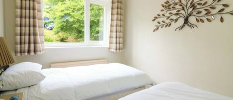 A bedroom with two beds, a window with curtains, a bedside lamp, and a wall decoration.