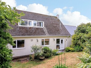A two-story house with a sloped roof, white exterior walls, and a small garden area with various plants and flowers. - 3 Chantry Hill (Kingsbridge)