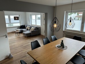 Una sala moderna con un sofá gris, una mesa de comedor de madera, sillas negras y lámparas colgantes.