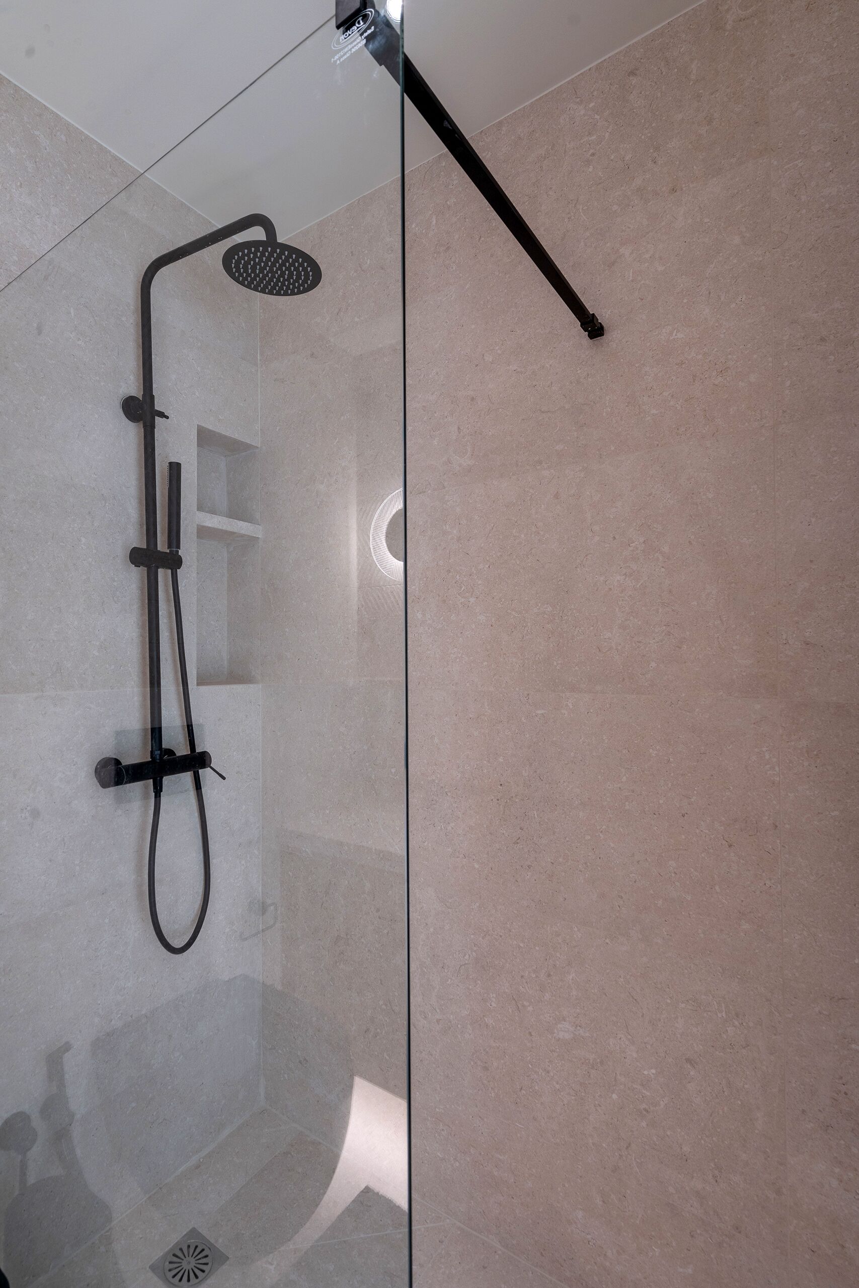 A modern shower with a glass enclosure, a handheld showerhead, and a wall-mounted control panel.