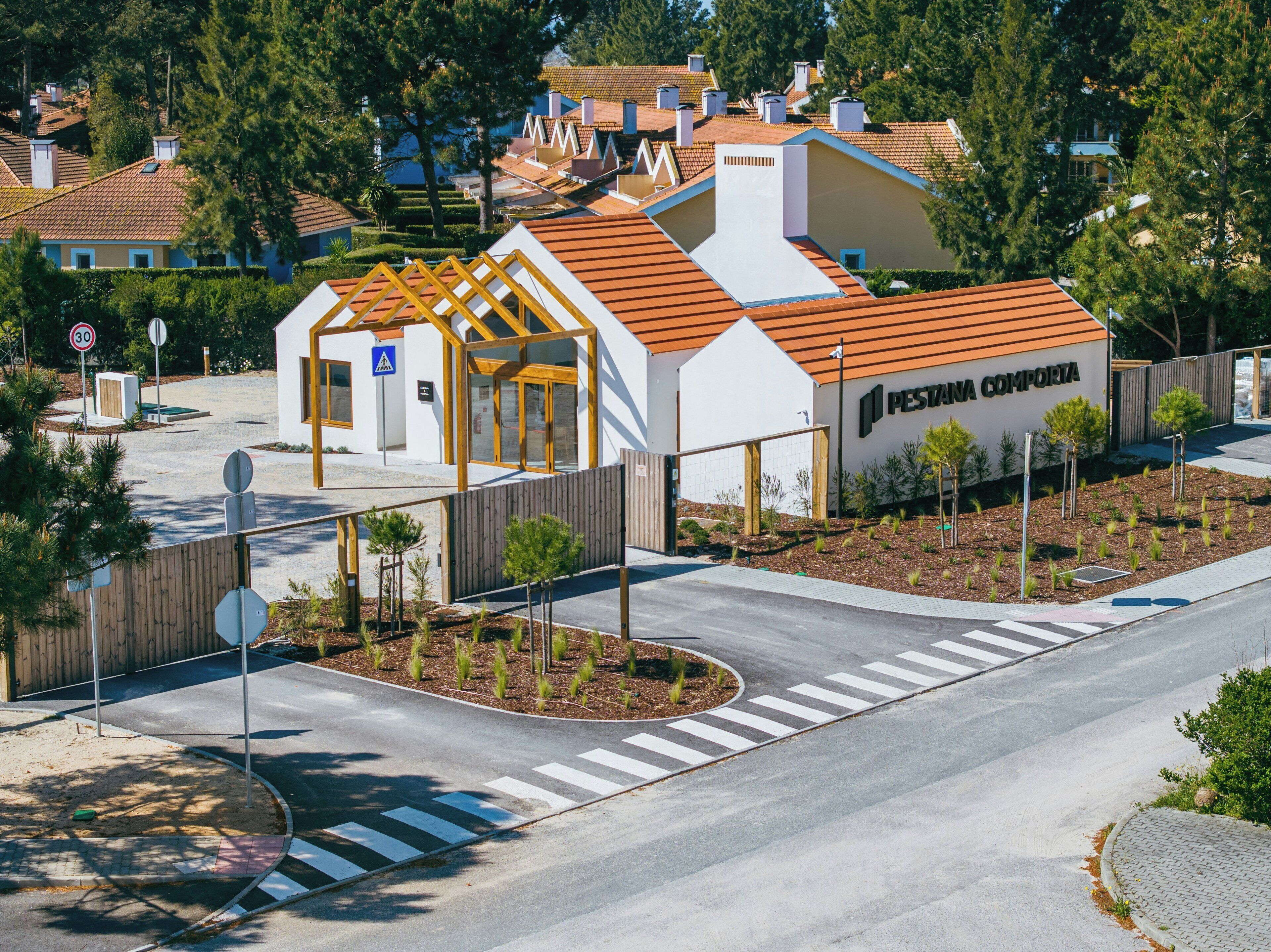 A modern building with a white facade and orange roof, featuring a pedestrian entrance and a sign reading 'PESTA NA COMPORTA'.
