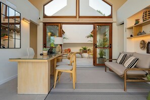 Een ruime zithoek met een grote glazen deur naar een balkon, een houten bureau en een comfortabele zithoek.