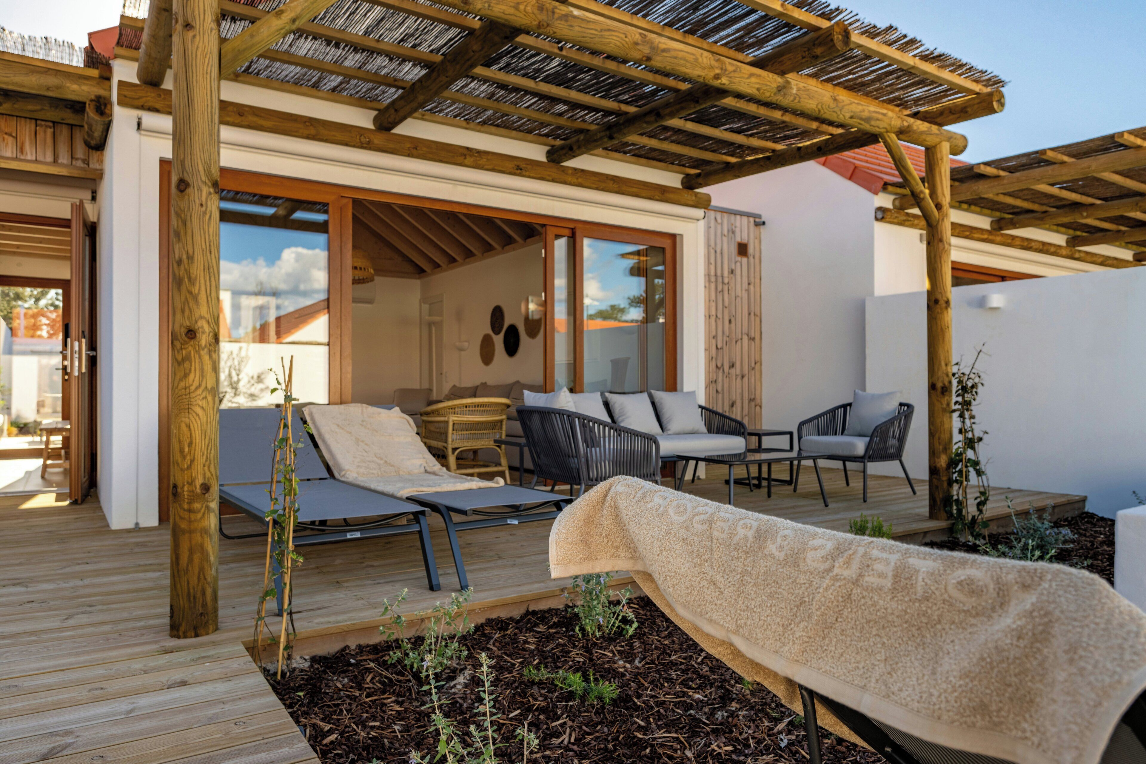 Une terrasse en bois avec des meubles d’extérieur, une pergola et une vue sur l’intérieur de la maison.