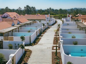 A row of modern, white-walled buildings with red-tiled roofs, arranged in a linear fashion along a central pathway.