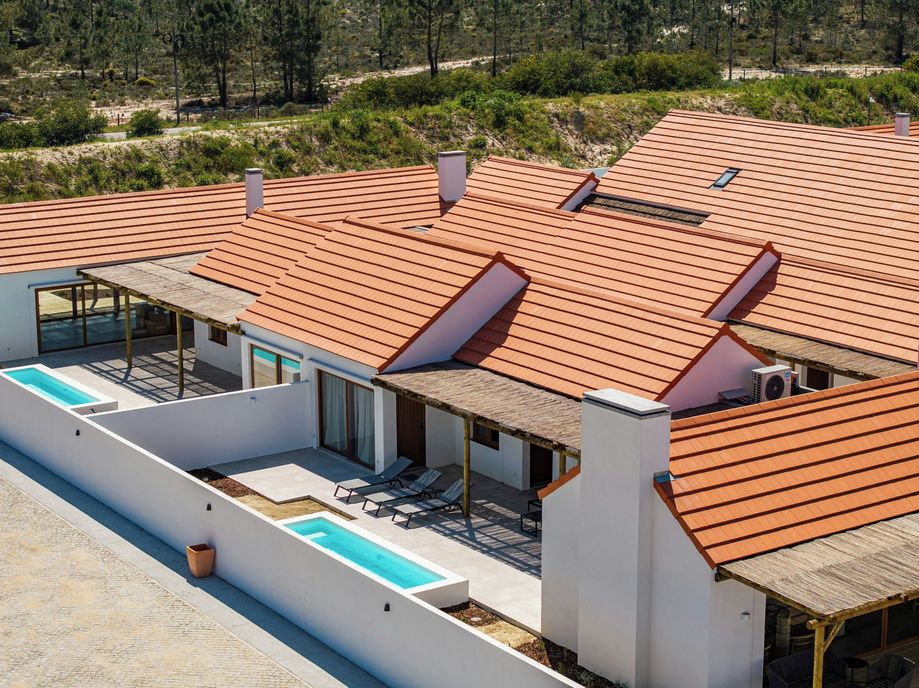 A modern house with a swimming pool, outdoor seating, and a red-tiled roof.