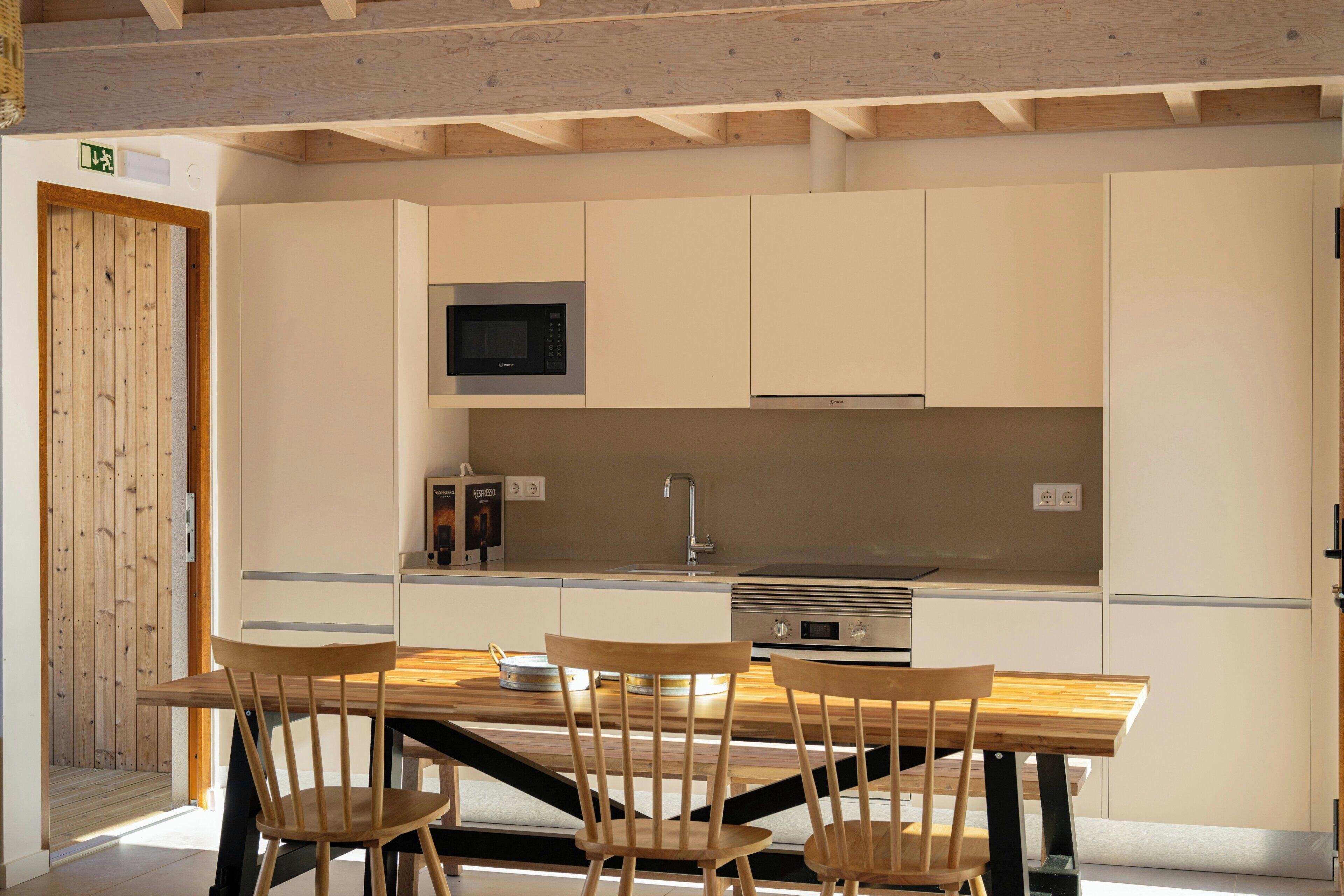 Una cocina moderna con gabinetes de madera, microondas integrado, cafetera y estufa. Cuatro sillas de madera rodean una mesa.