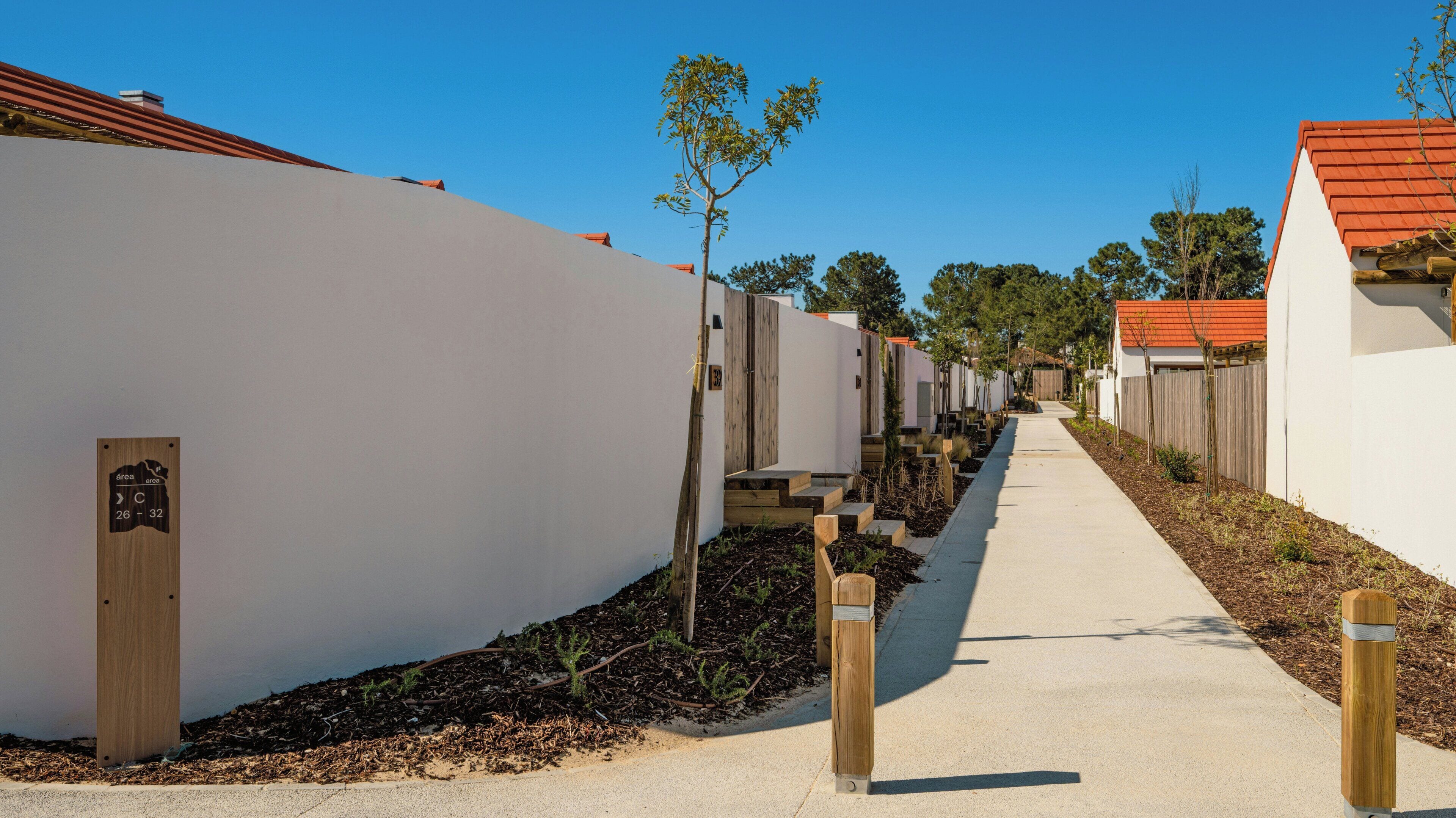 A pathway leading to a row of white buildings with red roofs, wooden steps, and a sign indicating room numbers 26-32.