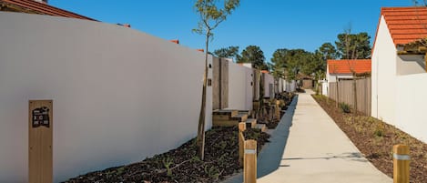 A pathway leading to a row of white buildings with red roofs, wooden steps, and a sign indicating room numbers 26-32.