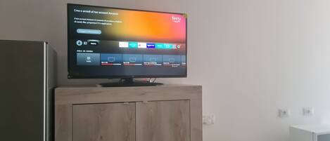 Een televisie op een houten kast, een digitale interface, een magnetron en een telefoon op een aanrecht.