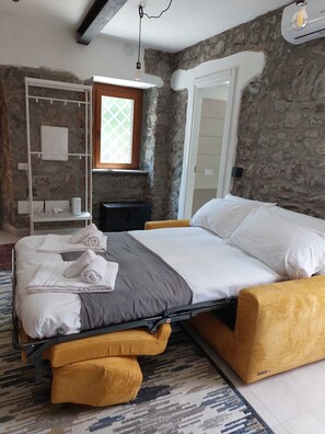 A bedroom with a bed, a wardrobe, a window, and a stone wall. - Il Rifugio delle Brunorie Etrusche (Montefiascone)