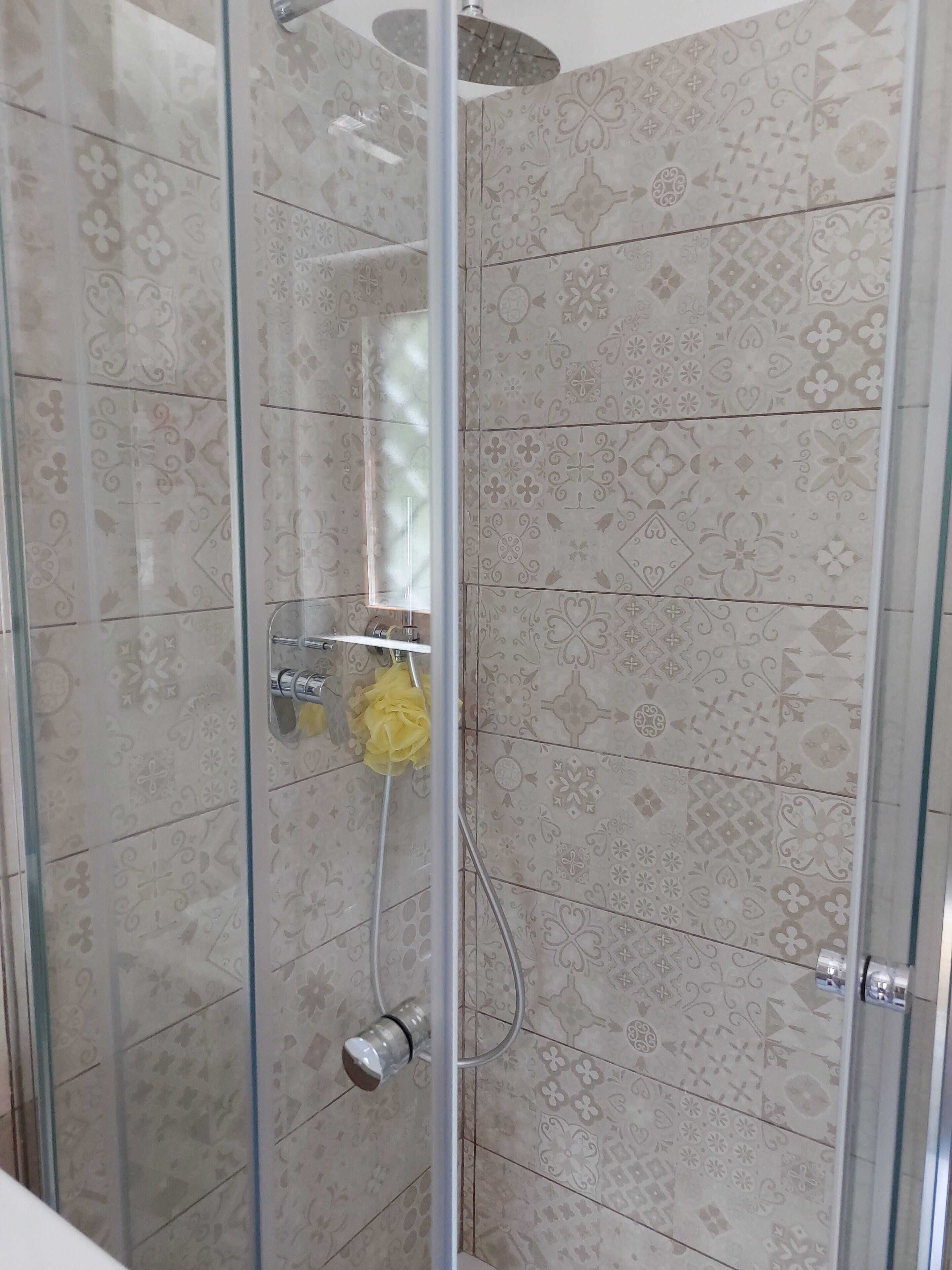 A shower with a glass door, a yellow bath sponge, and patterned tiles.