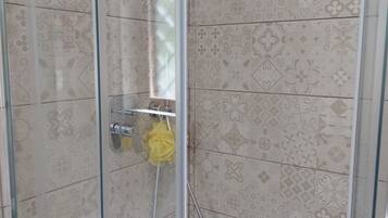 A shower with a glass door, a yellow bath sponge, and patterned tiles.