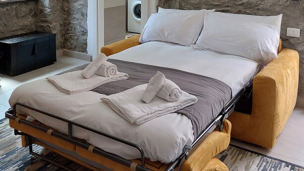A bedroom with a bed, a washing machine, and a stone wall.