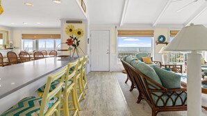 A spacious dining area with a long table and chairs, a balcony with a view, and a cozy seating area with cushions. - Oceanfront 6BR Getaway w/ Beach Access & Deck (Oak Island)