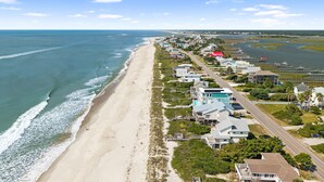 An aerial view of a coastal residential area with houses along the beach, a marina, and a road running parallel to the shore. - Oceanfront 6BR Getaway w/ Beach Access & Deck (Oak Island)