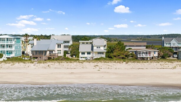 A beachfront property with multiple houses, a sandy beach, and a view of the ocean. - Oceanfront 6BR Getaway w/ Beach Access & Deck (Oak Island)