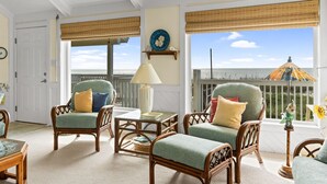 A cozy room with wicker chairs, a table, and a view of the ocean. - Oceanfront 6BR Getaway w/ Beach Access & Deck (Oak Island)
