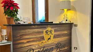 Un mostrador de recepción con detalles de madera, un logotipo con un ciervo y una corona, y el texto "Residencia Riva Wellness Apartment Spa".