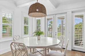 A dining area with a round table, white chairs, a hanging wicker light fixture, and a potted plant. - 4BR Luxury Home with Private Heated Pool + Elevator | White Sand Escape (Destin)
