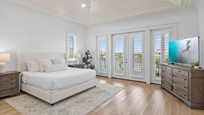 A bedroom with a large bed, a dresser, a television, and a view through the glass doors.